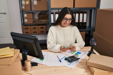 Young hispanic woman ecommerce business worker holding krone banknotes at office