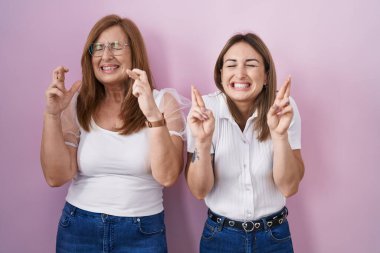 İspanyol anne ve kızı pembe arka planda gelişigüzel beyaz tişörtler giyip umut ve gözlerin kapalı gülümseyerek el kol hareketi yapıyorlar. Şans ve batıl inançlar. 