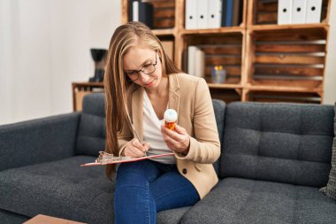 Young blonde woman psychologist prescribe pills at psychology clinic