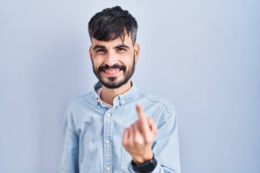 Mavi arka planda dikilen sakallı genç İspanyol adam, el hareketleriyle seni mutlu etmeye ve gülümsemeye çağırıyor. 