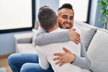 Two men couple hugging each other sitting on sofa at home