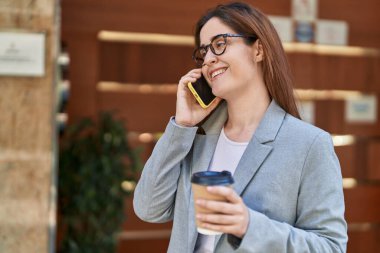 Genç iş kadını akıllı telefondan konuşuyor. Sokakta kahve içiyor.