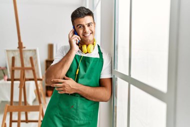 Genç İspanyol adam akıllı telefondan konuşuyor. Sanat stüdyosunun camına yaslanıyor.