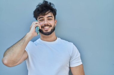 Genç İspanyol adam gülümsüyor. Akıllı telefondan beyaz izole edilmiş arka planda konuşuyor.