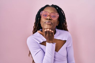 Pembe arka planda örülü saçları olan Afrikalı bir kadın havayla öpüşürken kameraya bakıyor. Güzel ve seksi. aşk ifadesi. 