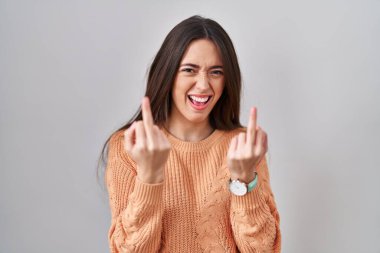 Young brunette woman standing over white background showing middle finger doing fuck you bad expression, provocation and rude attitude. screaming excited 