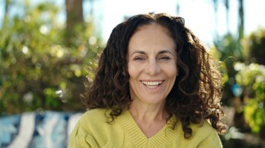 Orta yaşlı İspanyol kadın parkta kendinden emin gülümsüyor.