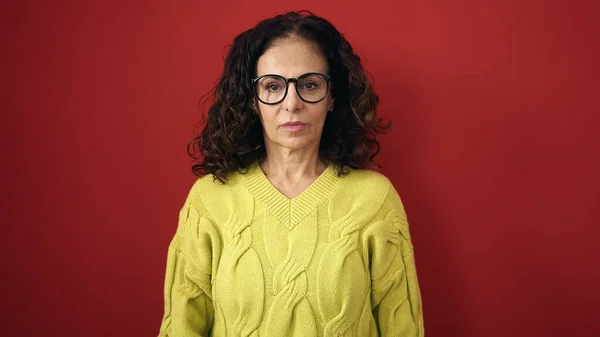 Middelbare Leeftijd Spaanse Vrouw Staan Met Ernstige Expressie Geïsoleerde Rode — Stockfoto
