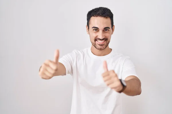 手で積極的なジェスチャーを行うことを承認白い背景の上に立ってハンサムなヒスパニック系の男 親指アップ笑顔と成功のために幸せ 勝者のジェスチャー — ストック写真