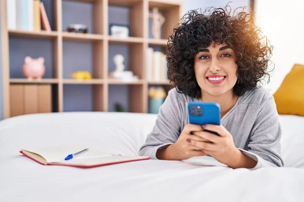 使用智能手机的年轻中东女人躺在卧室的床上 — 图库照片