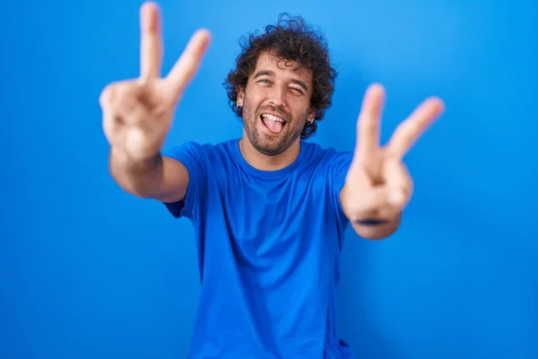Hispánský Mladík Stojící Nad Modrým Pozadím Usmívající Vyplazeným Jazykem Ukazujícím — Stock fotografie