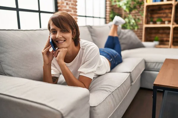 Young Beautiful Hispanic Woman Talking Smartphone Lying Sofa Home — Stockfoto