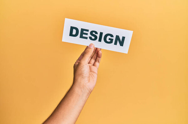 Hand of caucasian man holding paper with design word over isolated yellow background