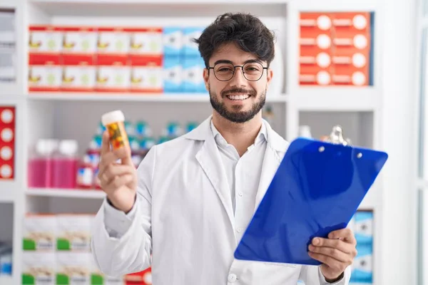 Jovem Hispânico Homem Farmacêutico Segurando Pílulas Garrafa Leitura Prescrição Farmácia — Fotografia de Stock