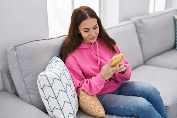 在家中使用智能手机的年轻女子坐在沙发上 — 图库照片