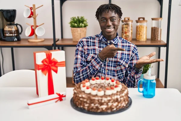 手で提示し 指で指している間にカメラに驚いて笑顔大きなチョコレートケーキを保持誕生日を祝うドレッドロックを持つアフリカの男 — ストック写真