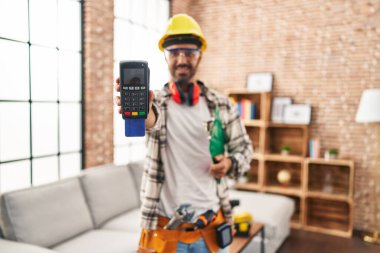 Genç İspanyol işçi gülümseyerek evde kredi kartıyla veri telefonu tutuyor.