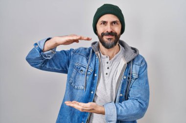 Dövmeli, yün şapkalı, elleri büyük ve büyük boy işareti olan İspanyol bir adam. Ölçü sembolü. Kameraya bakıp gülümsüyor. ölçüm kavramı. 