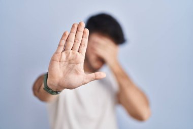 Beyaz arka planda sakallı İspanyol bir adam elleriyle gözlerini kapatıyor ve üzgün ve korku ifadeleriyle jestleri durduruyor. utangaç ve olumsuz kavram. 