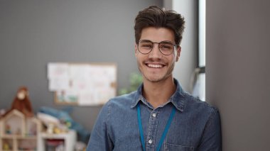 Young hispanic man preschool teacher smiling confident standing at kindergarten