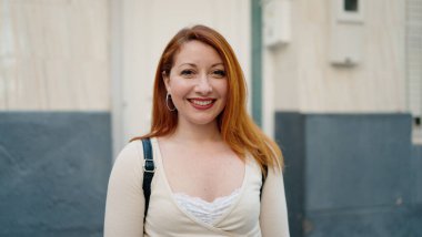 Caddede kendine güvenen genç kızıl saçlı kadın gülümsüyor