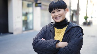 Sokakta kollarını kavuşturmuş genç Çinli bir kadın.