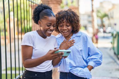 Afrika kökenli Amerikalı kadın anne ve kız sokakta akıllı telefondan video izliyorlar.