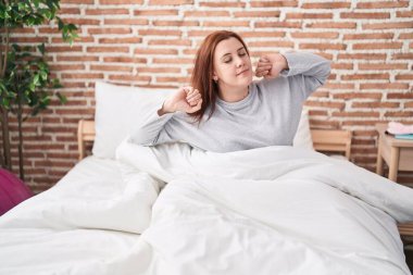 Young beautiful plus size woman waking up stretching arms at bedroom