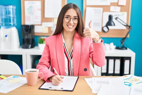 在办公室里工作的年轻的惊慌失措的女人戴着眼镜 赞成用手做积极的手势 微笑着竖起大拇指 为成功感到高兴 优胜手势 — 图库照片