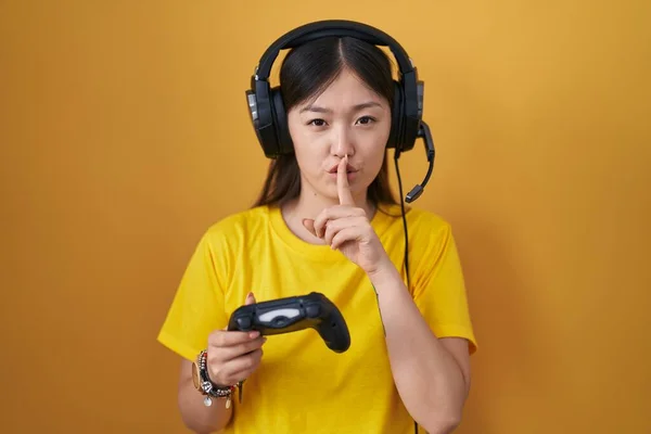 中国的年轻女子正在玩电子游戏 手持控制器 要求保持安静 手指放在嘴唇上 沉默和秘密概念 — 图库照片