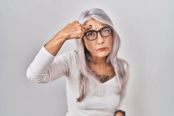白髪が白い背景の上に立っている中年の女性は額ににきび 黒頭の醜い感染に不幸な指している にきびや皮膚の問題 — ストック写真