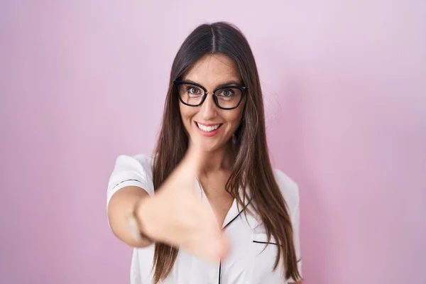 年轻的黑发女人戴着眼镜站在粉色背景上 友好地握手致意和欢迎 成功的商业 — 图库照片