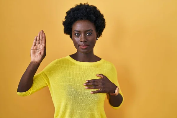 Afrykańska Młoda Kobieta Stojąca Nad Żółtym Studiem Przeklinająca Ręką Piersi — Zdjęcie stockowe