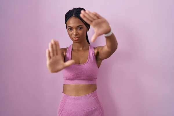 戴辫子 身穿运动服 背景粉红的非洲裔美国妇女用手心 手指头和相机透视画框 — 图库照片