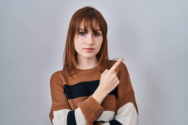 年轻漂亮的女人穿着条纹毛衣 披着孤立的背景 手指头指向广告的侧面 严肃而沉着 — 图库照片