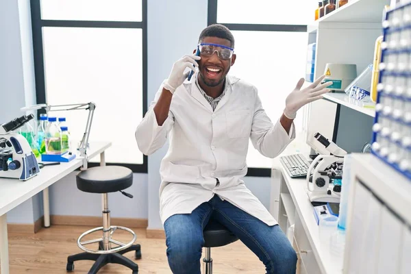 科学研究所で働くアフリカ系アメリカ人男性が幸せな笑顔で達成を祝う電話で話し 手を上げて勝者の表情 — ストック写真
