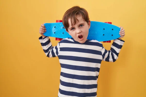Menino Caucasiano Segurando Skate Sobre Fundo Amarelo Rosto Choque Parecendo — Fotografia de Stock