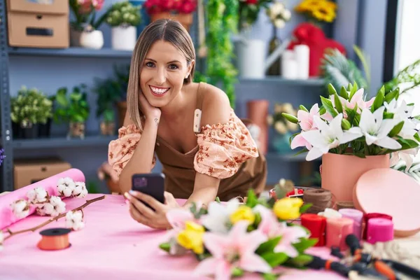 年轻美丽的惊慌失措的女花匠在花店用智能手机靠在桌子上 — 图库照片