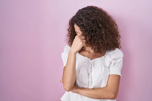 ピンクの背景に立っている巻き毛を持つヒスパニック系の女性は 鼻と目の疲労感や頭痛をこすり疲れている ストレスとフラストレーションの概念 — ストック写真