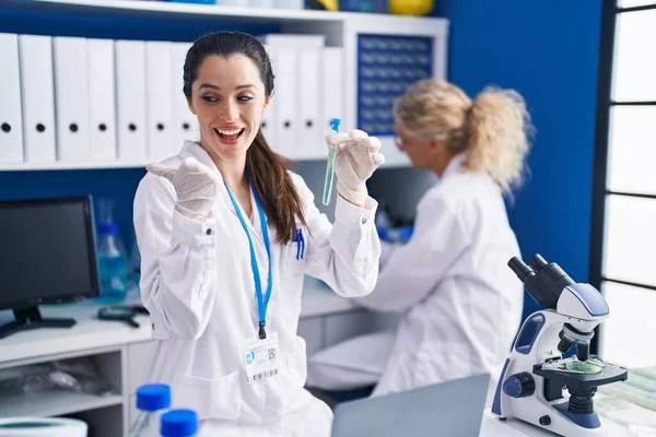 年轻的惊慌失措的女人在科学家实验室里工作 她把大拇指指向一边 笑着张开了嘴 — 图库照片
