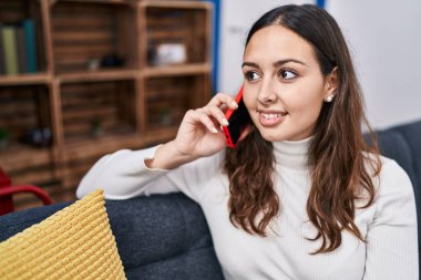 Evdeki kanepede oturmuş akıllı telefondan konuşan genç, güzel İspanyol kadın.