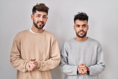 Beyaz arka planda el ele tutuşup gülümseyen rahat ve neşeli genç homoseksüel çift. Başarı ve iyimserlik 