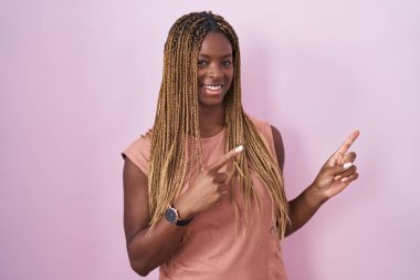 Pembe arka planda örülü saçları olan Afrikalı Amerikalı kadın gülümsüyor ve kameraya bakıyor.. 