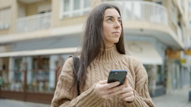 Kahve dükkanının terasında akıllı telefon kullanan genç ve güzel bir İspanyol kadın.