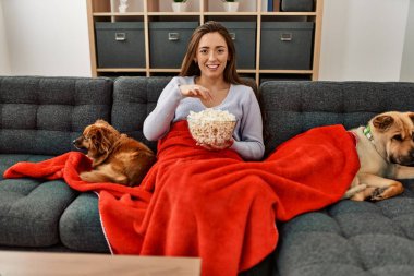 Genç İspanyol kadın evde köpeklerle kanepede oturup film izliyor.