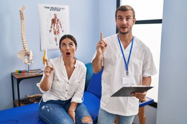 Fizyoterapistin randevusundaki genç İspanyol kadın şaşırmış ve şaşırmış bir şekilde yukarı baktı ve parmaklarıyla işaret ederek kollarını kaldırdı.. 