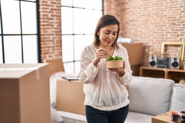 Orta yaşlı bir kadın yeni evinde salata yerken kendinden emin gülümsüyor.