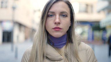 Young blonde woman standing with relaxed expression at street