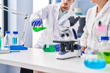 Young man and woman scientists workers measuring liquid at laboratory