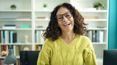 Orta yaşlı İspanyol kadın öğretmen kütüphanede kendine güvenen bir şekilde gülümsüyor.